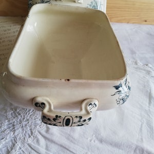 Op de afbeelding: Witte keramische serveerschaal met een blauw-wit bloemenmotief. De schaal heeft twee handvatten en een deksel.