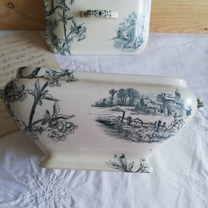 Op de afbeelding: Een witte keramische terrine met een blauw-wit bloemenpatroon. De terrine heeft een deksel met een bijpassend patroon en een handvat. De terrine staat op een wit tafelkleed.