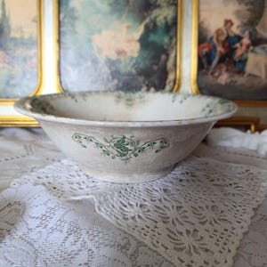 May include: A ceramic bowl with a wide, flared rim and a tapered base. The exterior features a light beige, mottled finish with a repeating green botanical vine pattern printed around the center and along the inner edge of the rim.