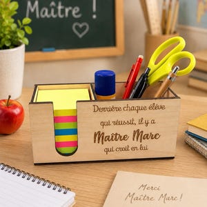 Peut inclure: Un organisateur de bureau rectangulaire en bois avec une découpe pour un bloc de notes adhésives néon. La face avant est gravée avec le texte : Derrière chaque élève qui réussit, il y a Maître Marc qui croit en lui. Il contient des stylos et des ciseaux.