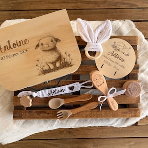 Peut inclure: Un coffret cadeau pour bébé en bois sur le thème de l'agneau. L'ensemble comprend une boîte, un hochet, une plaque ronde, une cuillère, une fourchette et un attache-tétine. La boîte est gravée du nom "Antoine" et de la date "02 Février 2026".