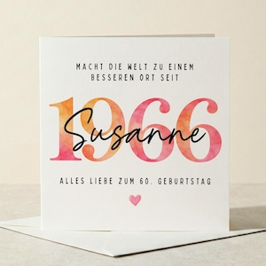 Könnte beinhalten: Eine weiße Grußkarte mit dem Text "MACHT DIE WELT ZU EINEM BESSEREN ORT SEIT 1966 Susanne ALLES LIEBE ZUM 60. GEBURTSTAG" in Schwarz, Orange und Rosa. Unten befindet sich ein kleines rosa Herz. Die Karte liegt auf einem weißen Umschlag.