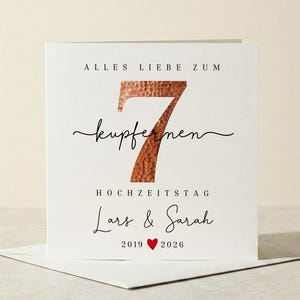 Könnte beinhalten: Eine weiße Grußkarte mit dem Text "ALLES LIEBE ZUM 7 KUPFERNEN HOCHZEITSTAG Lars & Sarah 2019 ❤️ 2026". Die Zahl 7 ist kupferfarben. Die Karte liegt auf einem weißen Umschlag.