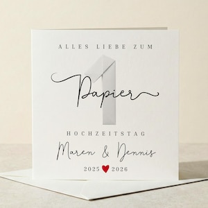 Könnte beinhalten: Eine weiße Papier-Jubiläumskarte mit dem Text "Alles Liebe zum Papier" und "Hochzeitstag Maren & Dennis 2025 ❤️ 2026" in schwarzer Schrift. Die Karte zeigt eine stilisierte Eins und liegt auf einem weißen Umschlag.