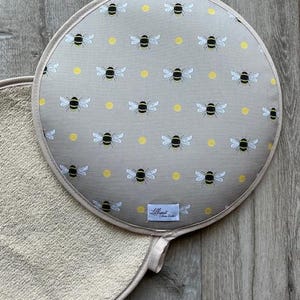 Peut inclure: Un dessous de plat rond, gris et blanc avec un motif d'abeilles et de points jaunes. Le dessous de plat est doté d'un dos en tissu éponge blanc.