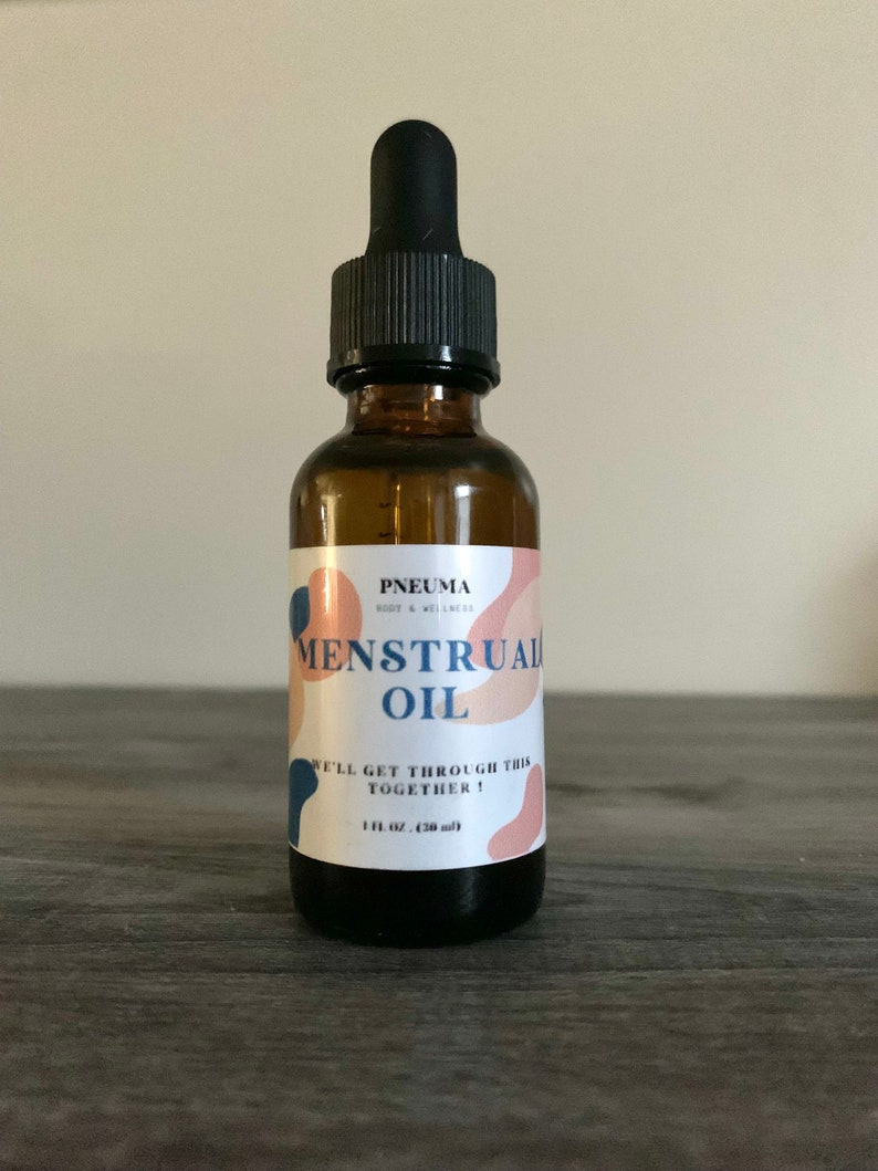 May include: A brown glass bottle with a black dropper top. The label is white with pink and blue abstract shapes and the text "PNEUMA BODY & WELLNESS MENSTRUAL OIL WE'LL GET THROUGH THIS TOGETHER! 1 fl oz (30 ml)"