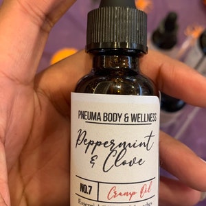 May include: A brown glass bottle with a black dropper top and a white label. The label reads "PNEUMA BODY & WELLNESS Peppermint & Clove NO.7 Cramp Oil Essential Oil Blend for aches and pains 1 OZ."