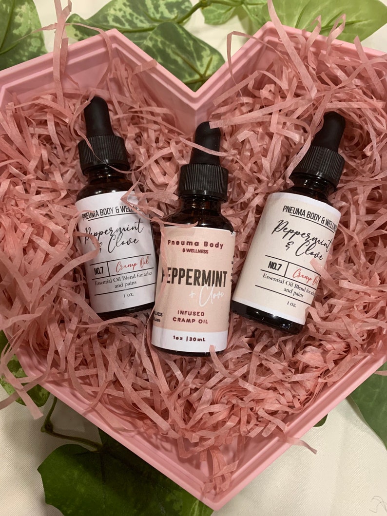May include: Two small brown glass bottles with dropper tops, filled with essential oil blends. The bottles are labelled "Peppermint & Clove" and "Peppermint + Clove Infused Cramp Oil". The bottles are in a pink heart-shaped box with pink crinkle paper.