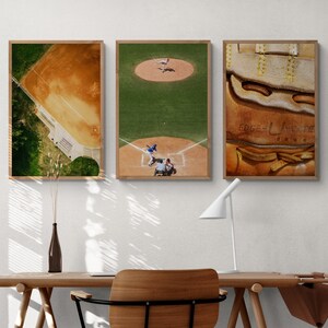K&ouml;nnte beinhalten: Drei gerahmte Baseball-Prints an einer wei&szlig;en Wand &uuml;ber einem Holztisch mit einem Stuhl. Die Prints zeigen eine Luftaufnahme eines Baseballfeldes, einen Baseballspieler, der in die Home Plate rutscht, und eine Nahaufnahme eines Baseballhandschuhs.