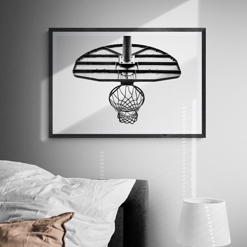 May include: Black and white photograph of a basketball hoop with a net. The hoop is mounted on a white wall. The image is framed in a black frame.