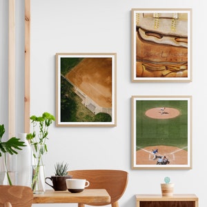 K&ouml;nnte beinhalten: Drei gerahmte Baseball-Prints. Der obere Druck zeigt eine Nahaufnahme eines braunen Leder-Baseballhandschuhs mit wei&szlig;en N&auml;hten und dem Text "Edge & Leather" in Wei&szlig;. Der mittlere Druck zeigt eine Luftaufnahme eines Baseballfeldes mit gr&uuml;nem Gras und einem braunen Innenfeld. Der untere Druck zeigt ein laufendes Baseballspiel mit Spielern in blauen und wei&szlig;en Uniformen auf einem gr&uuml;nen Feld.