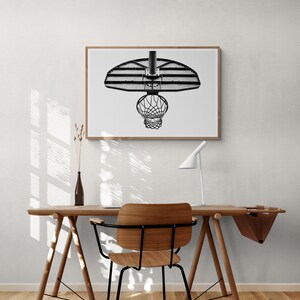 May include: A black and white photograph of a basketball hoop hanging from the ceiling. The hoop is in focus, while the background is blurred. The photo is framed in a wooden frame.