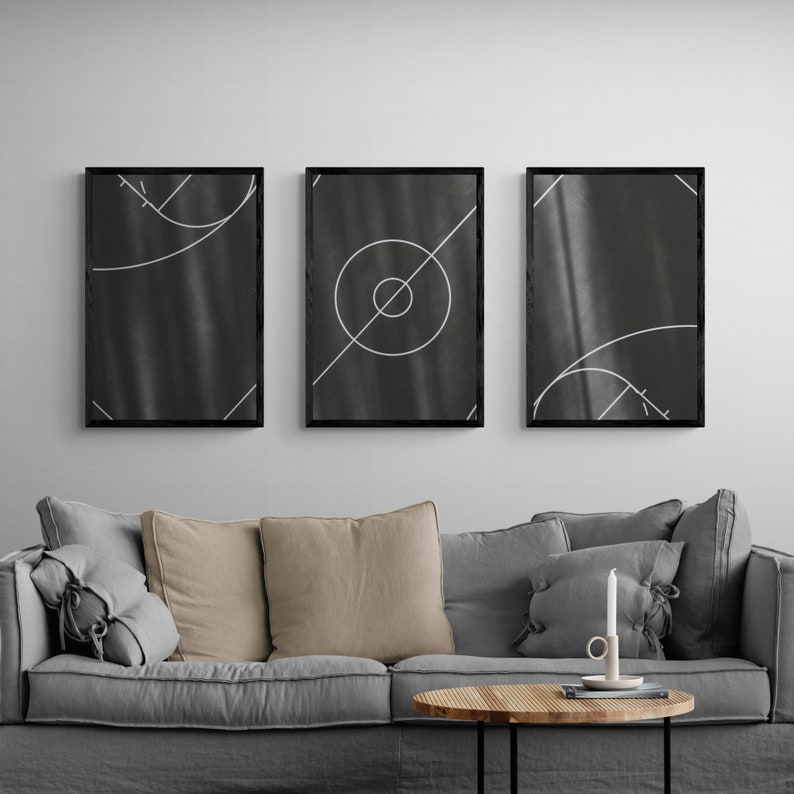 May include: Three black framed prints with white geometric designs on a dark gray background. The prints are hanging on a white wall above a gray couch with brown throw pillows.