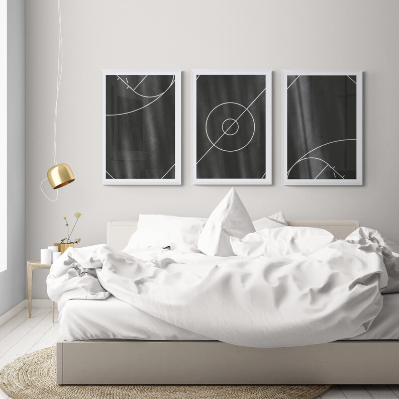 May include: Three black and white geometric abstract art prints in white frames hanging above a white bed with white bedding.
