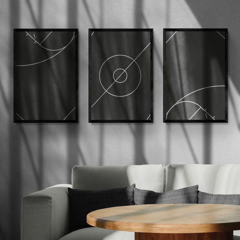 May include: Three black framed prints with white geometric designs on a black background. The prints are hanging on a white wall with shadows from a window. A white couch with gray pillows and a wooden table are in the foreground.