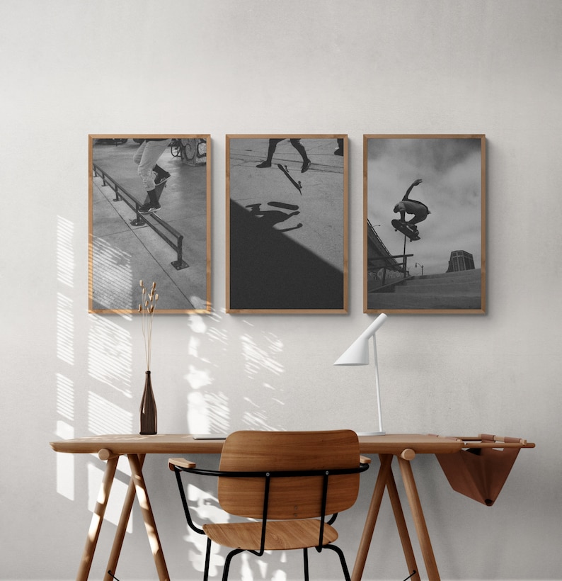 Puede incluir: Tres fotograf&iacute;as en blanco y negro enmarcadas de patinadores haciendo trucos. Las fotos est&aacute;n colgadas en una pared blanca sobre un escritorio de madera con una silla.