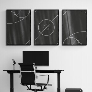 May include: Three black framed prints with white geometric designs on a black background. The prints are hanging on a white wall above a black desk with a black computer monitor, a black chair, and a black speaker.