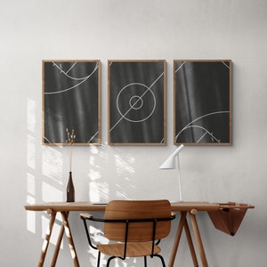 May include: Three black and white abstract art prints with geometric shapes and lines in a wooden frame. The prints are hanging on a white wall above a wooden desk with a chair and a lamp.