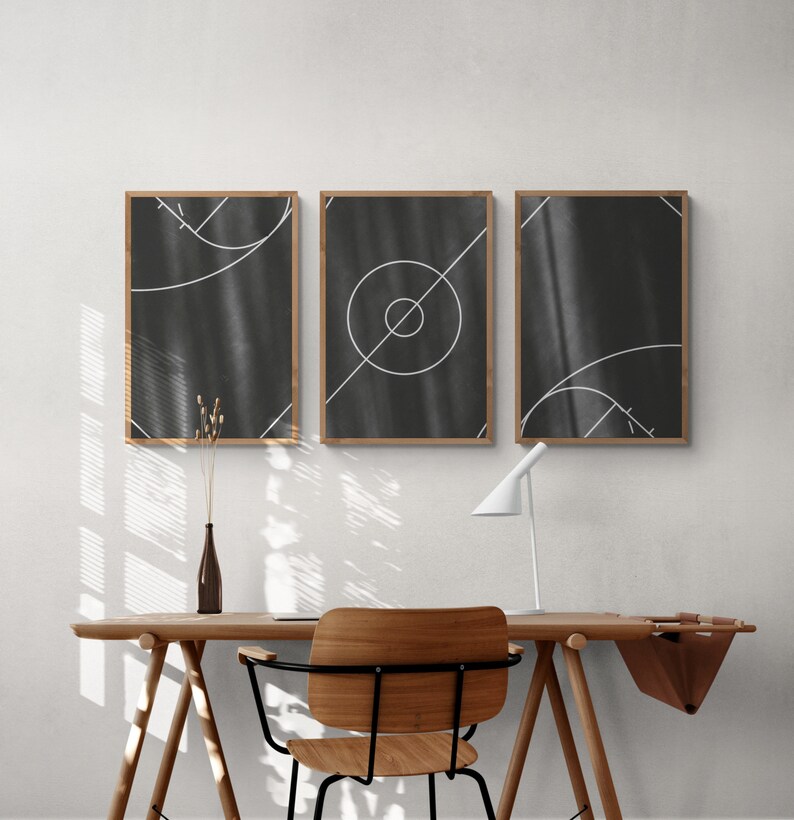 May include: Three black and white abstract art prints with geometric shapes and lines in a wooden frame. The prints are hanging on a white wall above a wooden desk with a chair and a lamp.