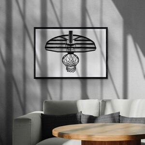 May include: Black and white photograph of a basketball hoop with a net hanging from it. The hoop is mounted on a wall and the net is hanging down. The photo is framed in a black frame.