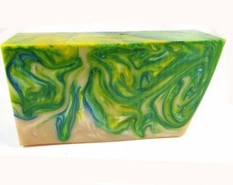 May include: A rectangular bar of handmade soap with a marbled design. The soap features swirls of green, yellow, and blue colors. The bottom portion of the soap is a light beige color. The soap is set against a white background.