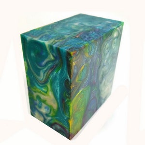 May include: A rectangular block with a swirling pattern of teal, green, yellow, and purple. The block has a polished, glossy finish, and the colors blend together in a marbled effect. The block is a solid, decorative item.