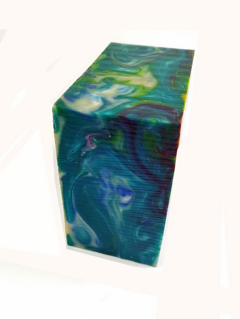 May include: A rectangular block of swirled resin in shades of teal, blue, green, and cream. The block has a polished surface with visible layers and a marbled effect. The colors blend together, creating a unique and artistic appearance.