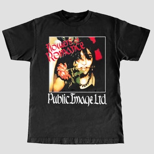 Op de afbeelding: Zwart T-shirt met een witte print van de albumhoes van "Flowers of Romance" van Public Image Ltd. De albumhoes toont een zwart-witfoto van een persoon met een roos in de mond.