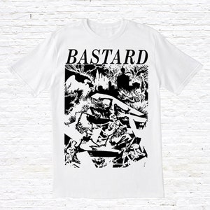 Op de afbeelding: Wit T-shirt met een zwart-witte grafische print van een donkere, gotische scène met het woord "BASTARD" in grote, vetgedrukte letters bovenaan.