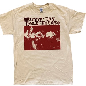 May include: A beige t-shirt with a red print of a band called "Sunny Day Real Estate". The print features a black and white image of two people playing guitars.