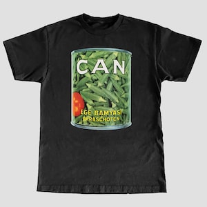 Może przedstawiać: Czarny T-shirt z grafiką puszki zielonej okry z czerwonym pomidorem. Na puszce widnieje napis "CAN" dużymi białymi literami oraz tekst "EGE BAMYASI OKRASCHOTEN" mniejszymi białymi literami.