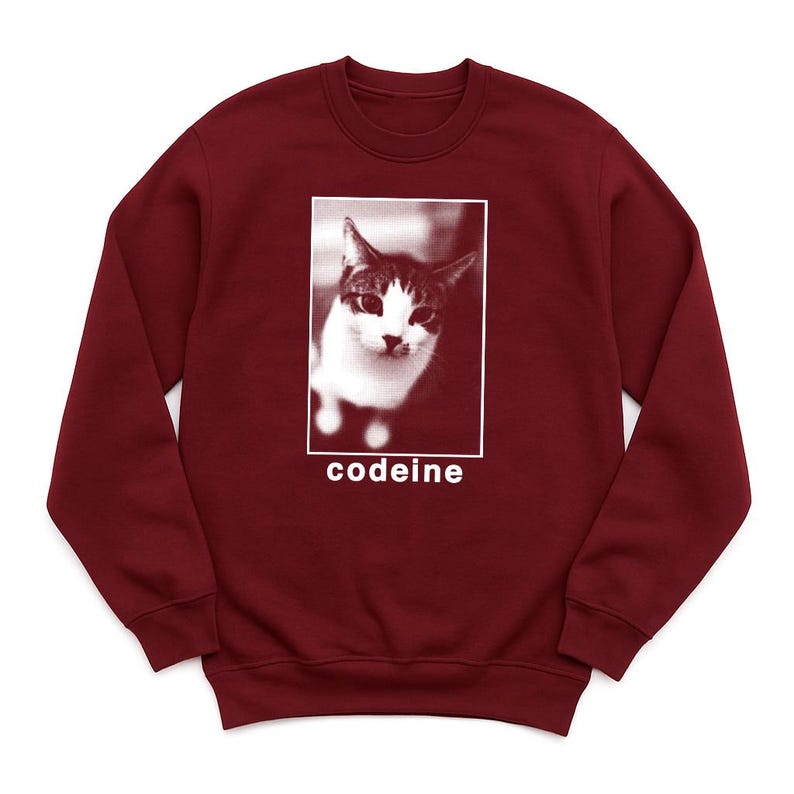 K&ouml;nnte beinhalten: Ein weinrotes Sweatshirt mit Rundhalsausschnitt und einem Schwarz-Wei&szlig;-Bild einer Katze in einem wei&szlig;en Rechteck. Das Wort "codeine" ist wei&szlig; unter dem Bild aufgedruckt. Das Sweatshirt ist aus weichem Material.