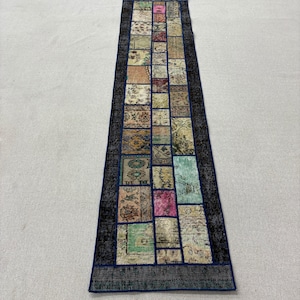 Könnte beinhalten: Ein rechteckiger Patchwork-Teppich mit dunkelblauem Rand und einem zentralen Design aus verschiedenen rechteckigen Flicken in gedämpften Farben. Die Flicken weisen florale und geometrische Muster auf und erzeugen eine Vintage-Ästhetik. Geeignet für einen Flur.