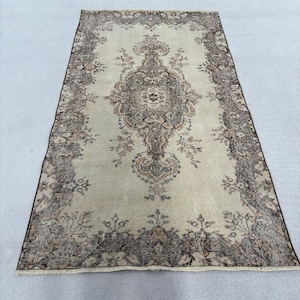 May include: A rectangular, vintage-style rug with a central medallion design. The rug features a cream-colored field with a detailed floral pattern in shades of brown and tan. The border is a darker brown with floral motifs.
