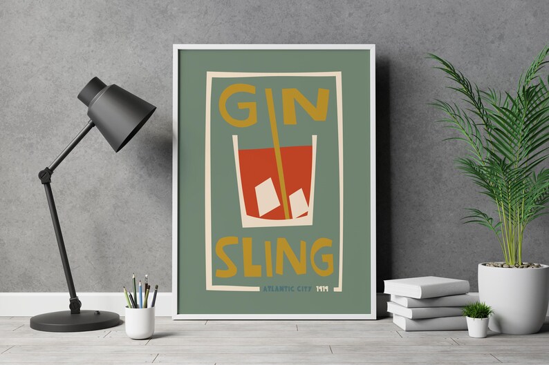Puede incluir: Una l&aacute;mina enmarcada con fondo verde salvia que presenta una ilustraci&oacute;n estilizada de un c&oacute;ctel rojo en un vaso con cubitos de hielo y una pajita amarilla. El texto GIN SLING est&aacute; impreso en amarillo, con ATLANTIC CITY 1919 en la parte inferior.
