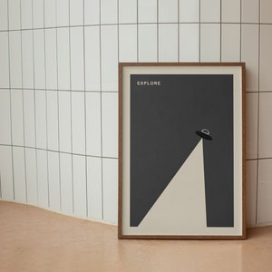 Puede incluir: Un p&oacute;ster enmarcado con un fondo gris oscuro y una forma triangular blanca con un OVNI negro en la parte superior. El p&oacute;ster tiene la palabra "EXPLORE" impresa en blanco en la parte superior.