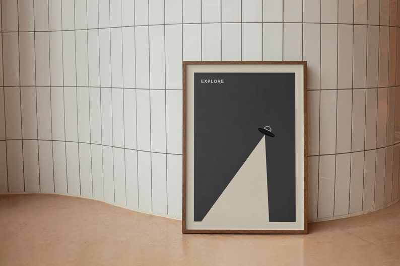 Puede incluir: Un p&oacute;ster enmarcado con un fondo gris oscuro y una forma triangular blanca con un OVNI negro en la parte superior. El p&oacute;ster tiene la palabra "EXPLORE" impresa en blanco en la parte superior.