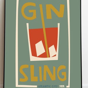 Puede incluir: Una l&aacute;mina enmarcada con fondo verde salvia que muestra un gr&aacute;fico estilizado de un c&oacute;ctel rojo en un vaso con dos cubitos de hielo blancos y una pajita amarilla. El texto GIN SLING est&aacute; impreso en amarillo, con ATLANTIC CITY 1919 debajo.