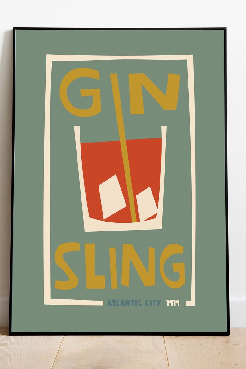 Puede incluir: Una l&aacute;mina enmarcada con fondo verde salvia que muestra un gr&aacute;fico estilizado de un c&oacute;ctel rojo en un vaso con dos cubitos de hielo blancos y una pajita amarilla. El texto GIN SLING est&aacute; impreso en amarillo, con ATLANTIC CITY 1919 debajo.
