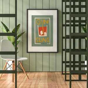 Puede incluir: Una l&aacute;mina de arte enmarcada con una ilustraci&oacute;n gr&aacute;fica de un c&oacute;ctel rojo en un vaso con cubitos de hielo y una pajita, con el texto GIN SLING en letras amarillas sobre un fondo verde suave dentro de un marco negro fino.