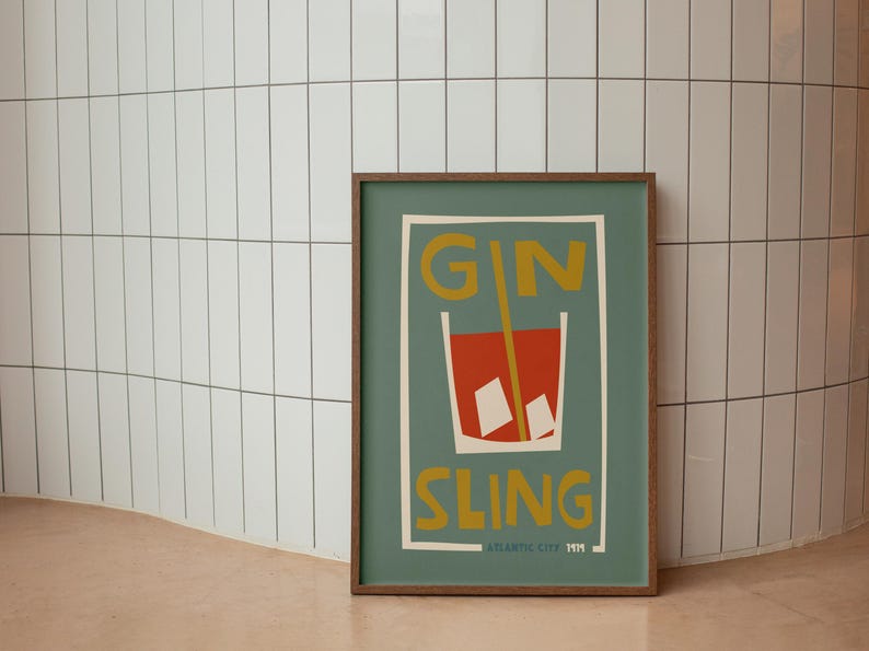 Puede incluir: Un p&oacute;ster rectangular enmarcado con fondo verde apagado que presenta una ilustraci&oacute;n estilizada de un c&oacute;ctel rojo en un vaso con cubitos de hielo y una pajita amarilla. El texto GIN SLING est&aacute; impreso en amarillo, con ATLANTIC CITY 1919 abajo.