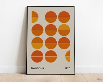May include: A framed poster featuring a beige background with a grid of orange and yellow circles, each divided horizontally. The text "bauhaus" and "1920" is printed in black at the bottom. The design uses geometric shapes in warm tones.