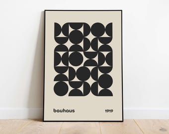 Op de afbeelding: Een rechthoekige wandkunstprint in een zwarte lijst met een beige achtergrond en een centraal raster van zwarte geometrische vormen, waaronder cirkels en halve cirkels. De tekst "bauhaus" staat linksonder en "1919" rechtsonder.