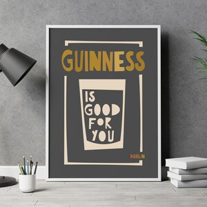 Op de afbeelding: Een zwart-witte poster met de tekst "GUINNESS IS GOOD FOR YOU" in een gouden lettertype. De poster bevat ook een glas Guinness met een witte achtergrond en het woord "DUBLIN" in een gouden lettertype.