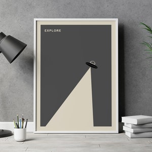 Puede incluir: Un p&oacute;ster enmarcado con un fondo gris oscuro y un borde blanco. El p&oacute;ster presenta una silueta negra de un platillo volante con un rayo de luz que brilla hacia abajo. El texto "EXPLORE" est&aacute; impreso en blanco en la parte superior del p&oacute;ster.