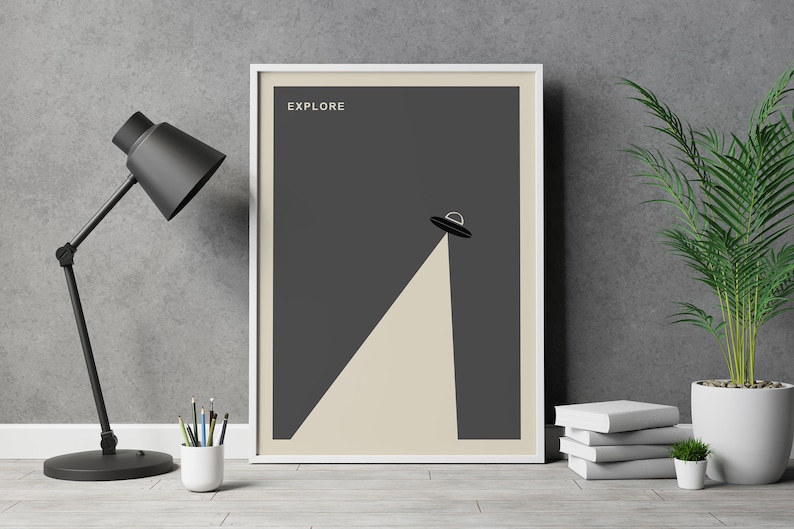 Puede incluir: Un p&oacute;ster enmarcado con un fondo gris oscuro y un borde blanco. El p&oacute;ster presenta una silueta negra de un platillo volante con un rayo de luz que brilla hacia abajo. El texto "EXPLORE" est&aacute; impreso en blanco en la parte superior del p&oacute;ster.