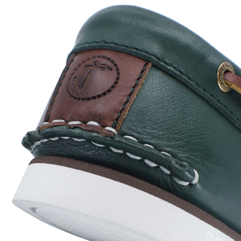 Puede incluir: Primer plano de un zapato n&aacute;utico de cuero verde con costuras blancas y un logotipo de ancla de cuero marr&oacute;n.