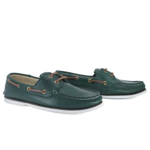 Puede incluir: Un par de zapatos n&aacute;uticos de cuero verde oscuro con suelas blancas y cordones marrones. Los zapatos tienen un logotipo de ancla dorada en el lateral.