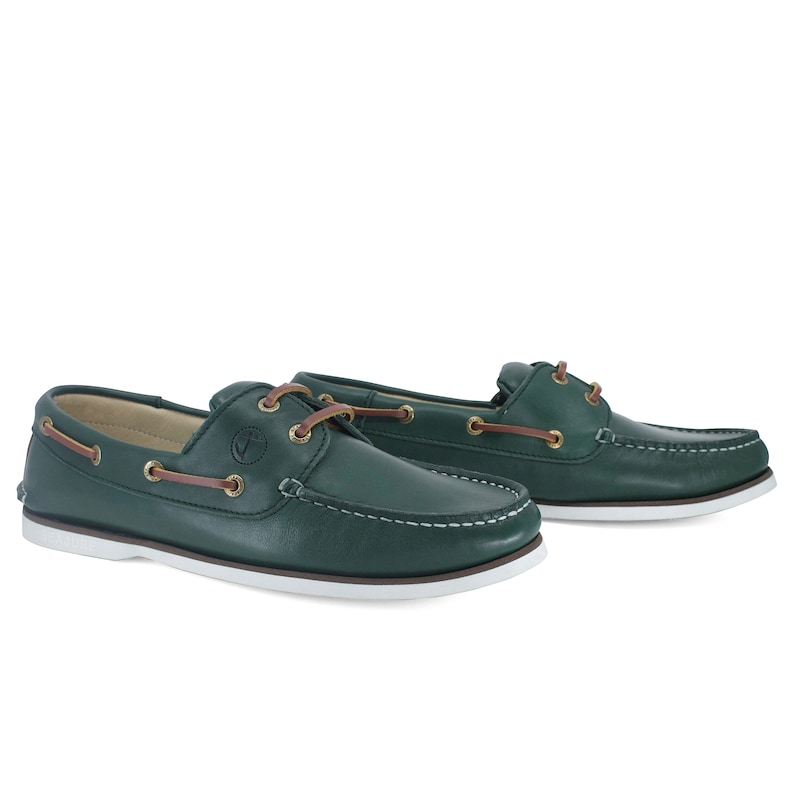 Puede incluir: Un par de zapatos n&aacute;uticos de cuero verde oscuro con suelas blancas y cordones marrones. Los zapatos tienen un logotipo de ancla dorada en el lateral.
