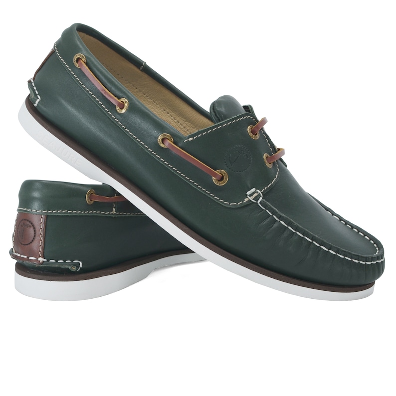 Puede incluir: Un par de zapatos n&aacute;uticos de cuero verde oscuro con cordones marrones y suelas blancas.